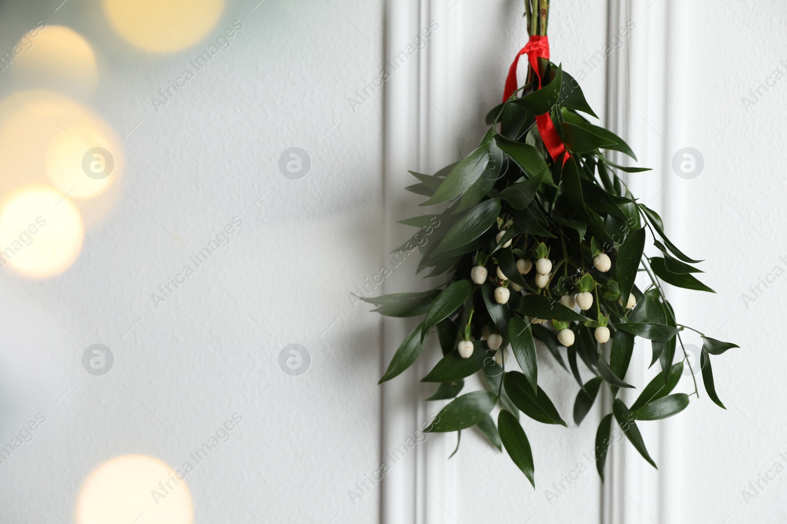 Photo of Mistletoe bunch with red ribbon hanging on light background, space for text. Bokeh effect