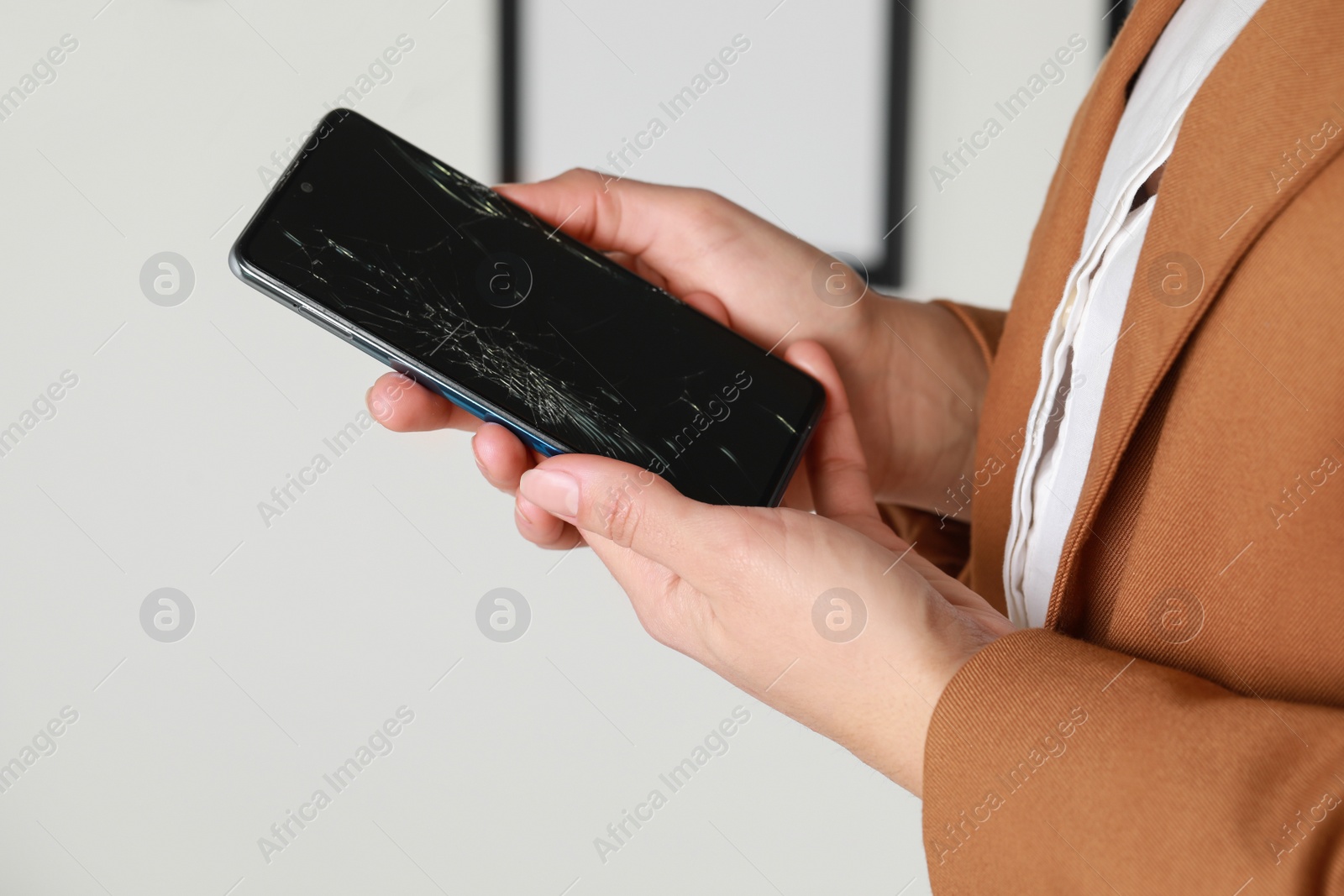 Photo of Woman holding damaged smartphone near white wall, closeup. Device repairing