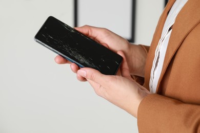 Photo of Woman holding damaged smartphone near white wall, closeup. Device repairing