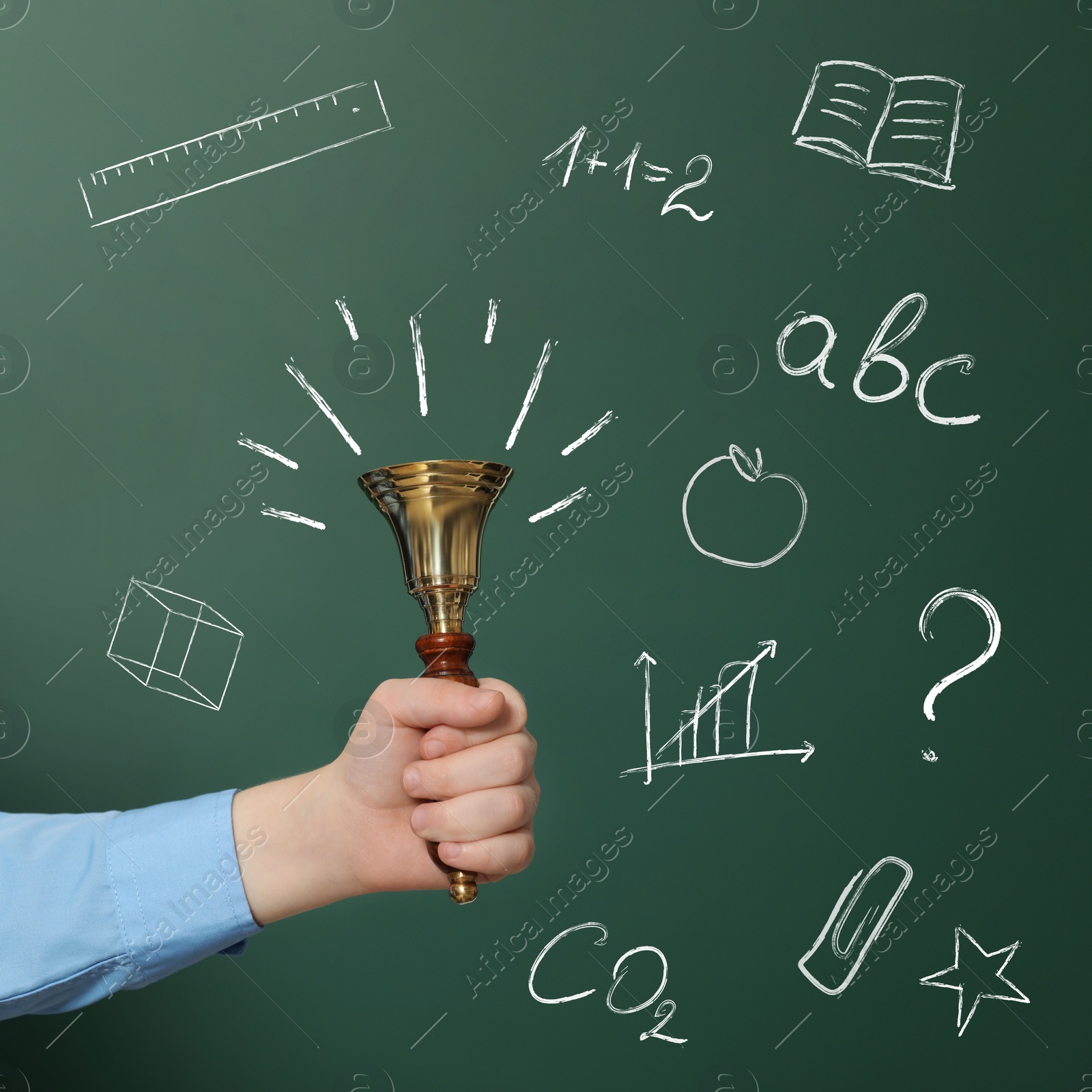 Image of Pupil holding school bell near green chalkboard with drawings and inscriptions, closeup