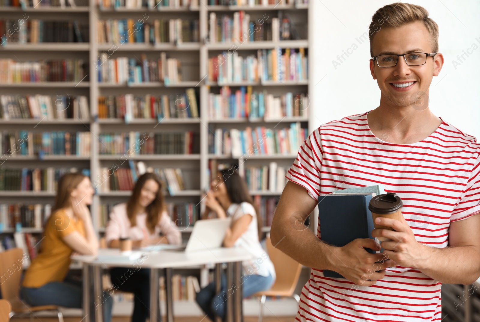 Photo of Young man with books and drink in library. Space for text