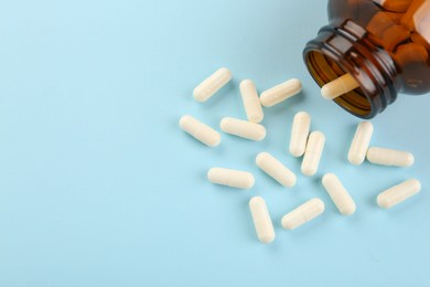 Photo of Bottle and vitamin capsules on light blue background, above view. Space for text