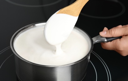 Woman cooking delicious creamy sauce in pan on stove, closeup