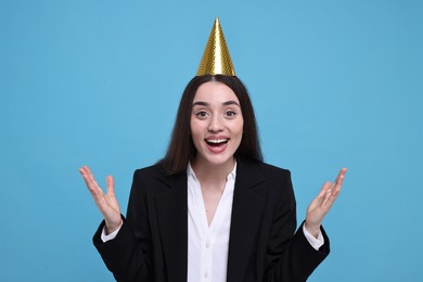 Happy woman in party hat on light blue background