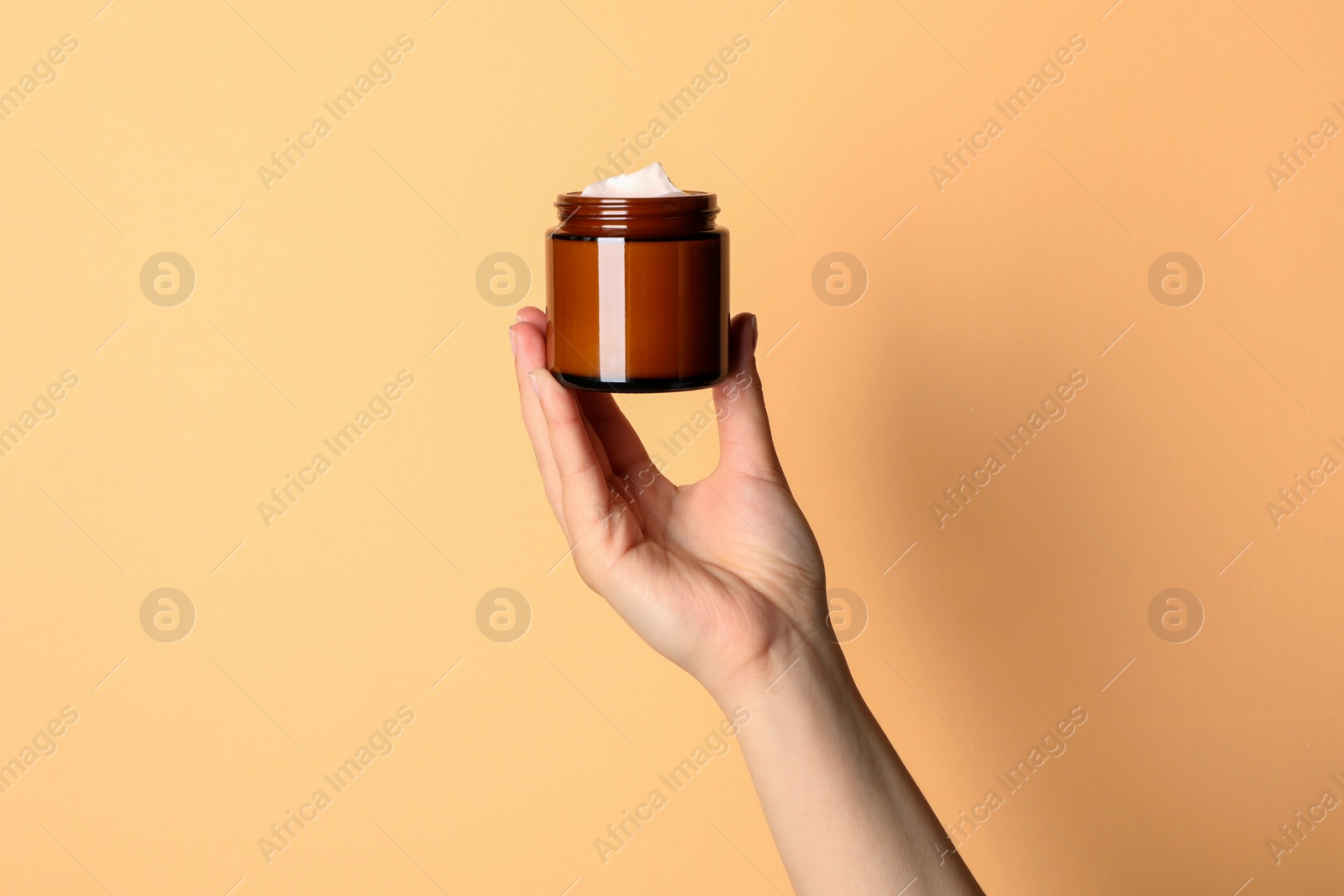 Photo of Woman holding jar of face cream on light orange background, closeup