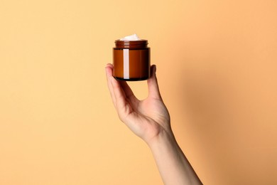 Photo of Woman holding jar of face cream on light orange background, closeup