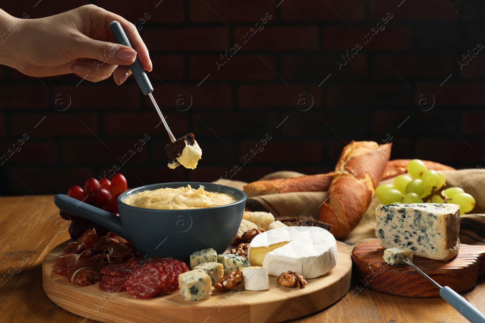 Photo of Woman dipping piece of bread into fondue pot with melted cheese at wooden table, closeup