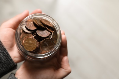 Photo of Woman holding donation jar with coins on light background, top view. Space for text