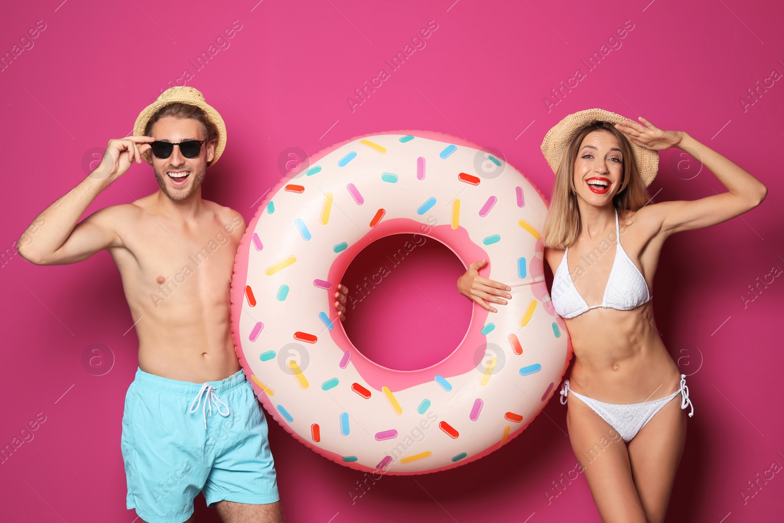 Photo of Happy young couple in beachwear with inflatable ring on color background