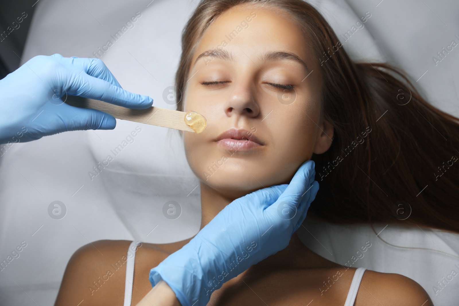 Photo of Young woman undergoing hair removal procedure on face with sugaring paste in salon