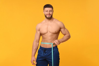 Photo of Athletic man measuring waist with tape on orange background. Weight loss concept