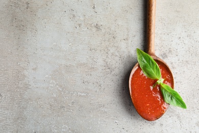 Photo of Spoon of tomato sauce on grey table, top view. Space for text