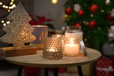 Burning candles on wooden table in room decorated for Christmas