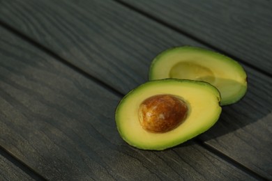 Photo of Halves of fresh avocado on wooden table. Space for text
