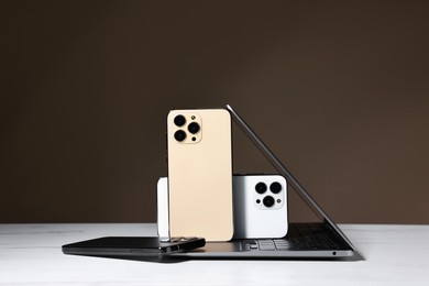 Photo of Modern laptop and smartphones on white table against brown background