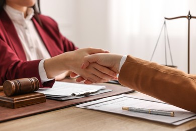 Photo of Notary shaking hands with client at wooden table in office, closeup