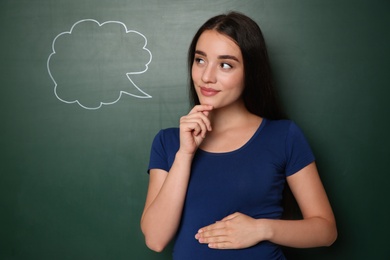 Photo of Pregnant woman thinking about baby name near green chalkboard