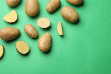 Photo of Fresh raw potatoes on green background, flat lay. Space for text