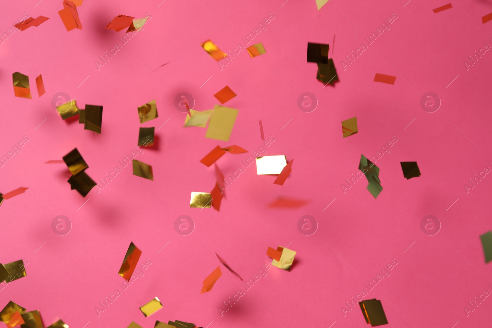 Photo of Shiny golden confetti falling down on pink background