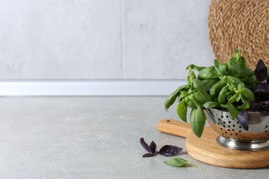 Photo of Metal colander with different fresh basil leaves on grey countertop, space for text