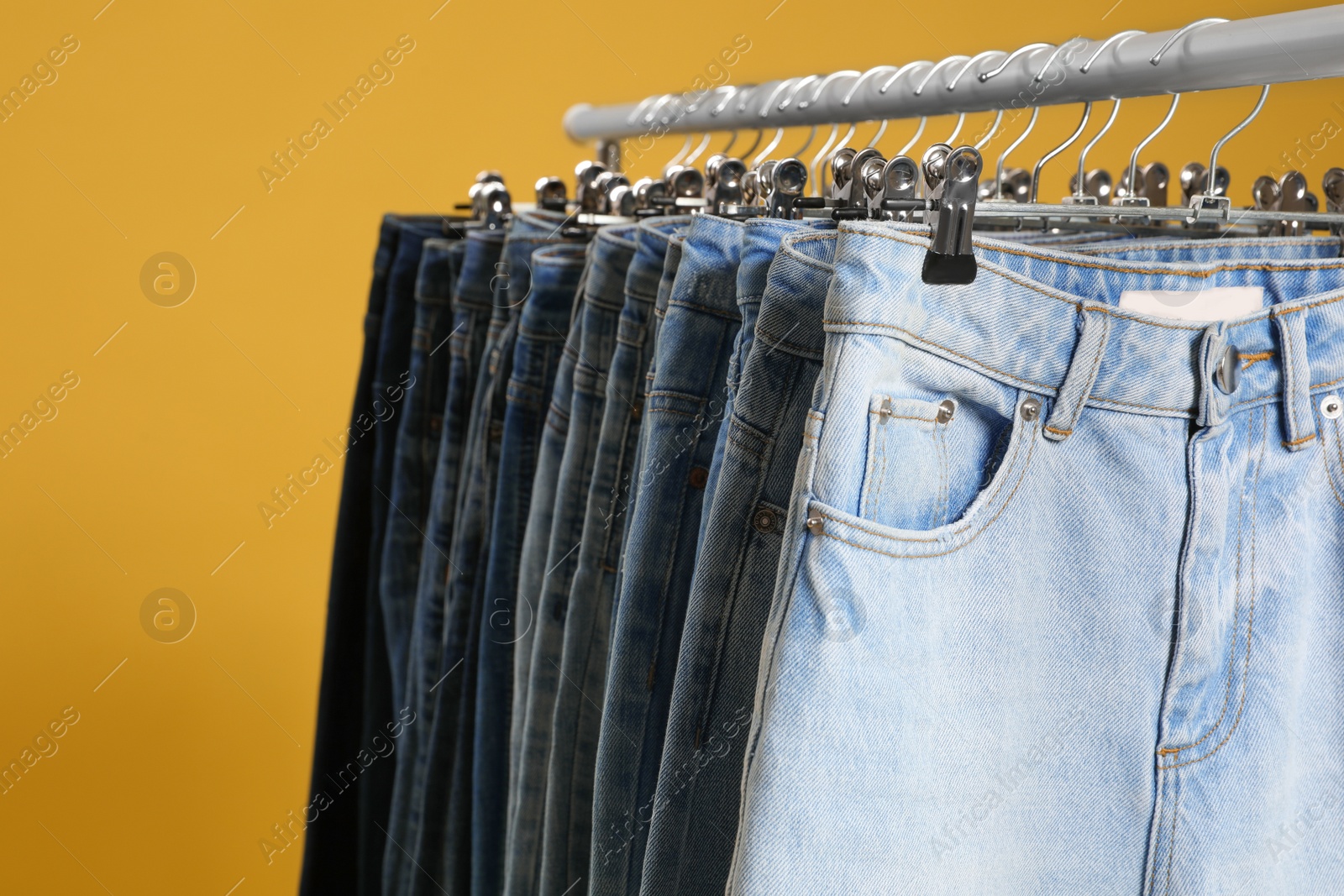 Photo of Rack with different jeans on yellow background, closeup