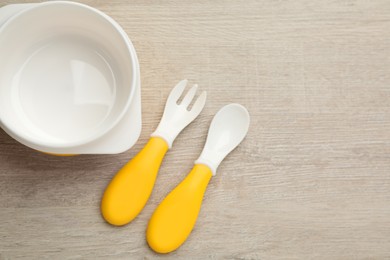 Plastic bowl and cutlery on wooden background, flat lay with space for text. Serving baby food