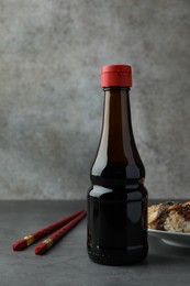 Photo of Bottle of tasty soy sauce, chopsticks and sushi on grey table