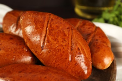 Photo of Delicious baked pirozhki on wooden board, closeup
