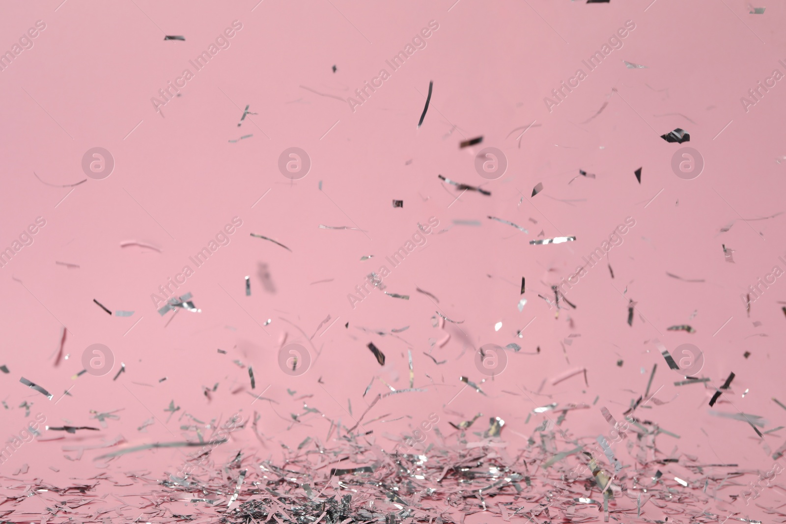 Photo of Shiny silver confetti falling down on pink background