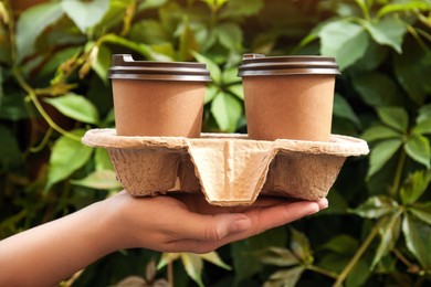 Photo of Woman holding cardboard holder with takeaway paper coffee cups outdoors, closeup