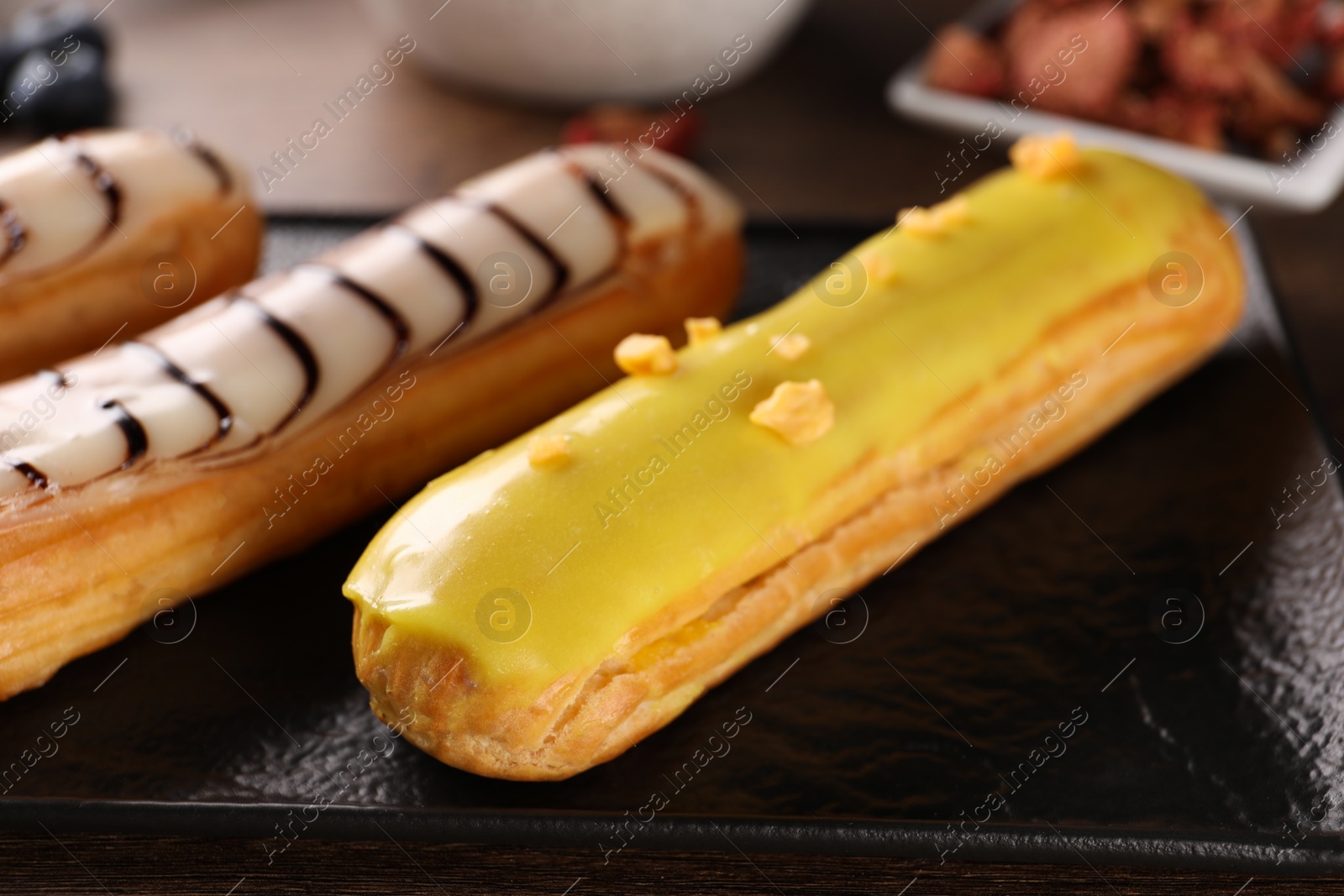 Photo of Plate with different tasty glazed eclairs on table, closeup