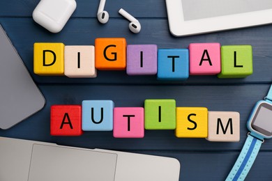 Phrase Digital Autism made of colorful cubes and devices on blue wooden table, flat lay. Addictive behavior