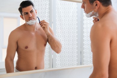 Photo of Handsome man shaving near mirror in bathroom