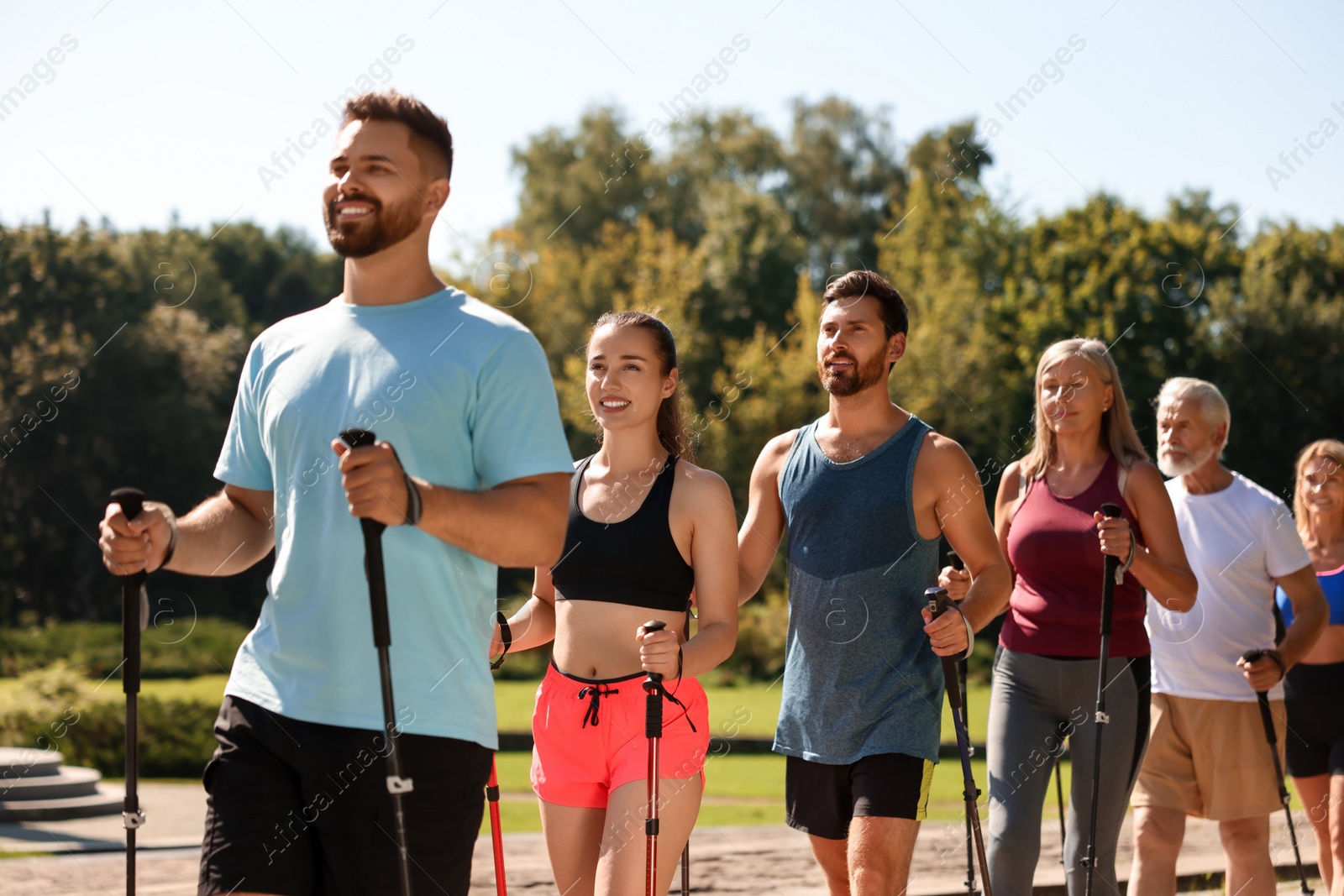 Photo of Group of people practicing Nordic walking with poles in park on sunny day