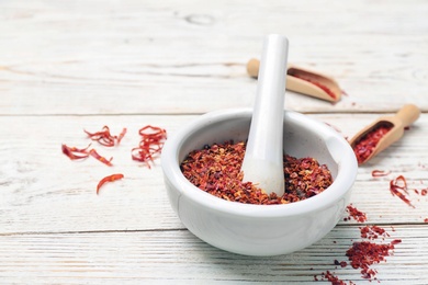 Ceramic mortar with chili pepper flakes on wooden background