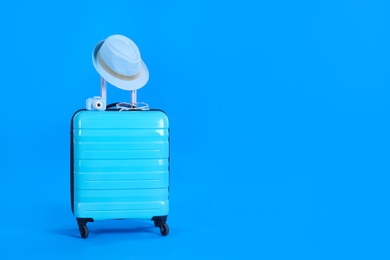 Photo of Travel suitcase with hat, camera and glasses on light blue background, space for text. Summer vacation