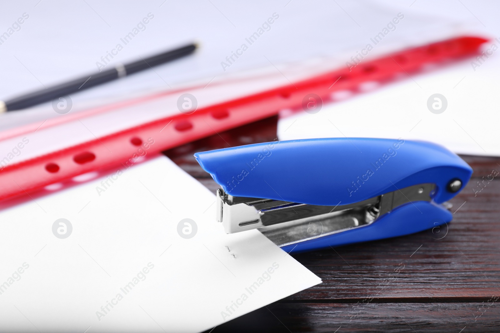 Photo of New bright stapler with paper sheet on wooden table, closeup