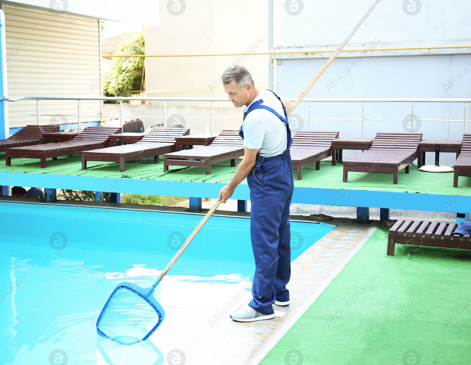 Photo of Male worker cleaning outdoor pool with scoop net