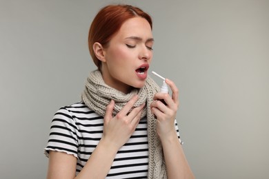 Photo of Young woman with scarf using throat spray on grey background