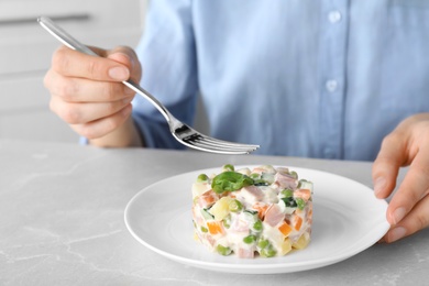 Young woman with delicious salad Olivier at light table, closeup