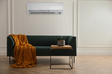 Image of Modern air conditioner on white wall in room with stylish green sofa