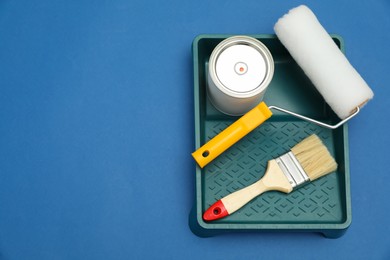 Photo of Can of orange paint, brush, roller and container on blue background, flat lay. Space for text