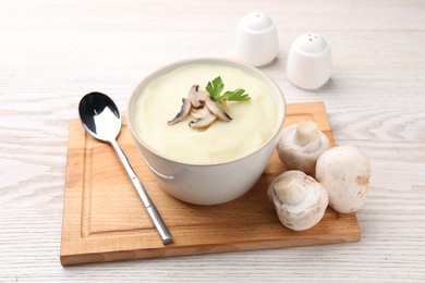 Bowl of tasty cream soup with mushrooms, parsley and spoon on light wooden table