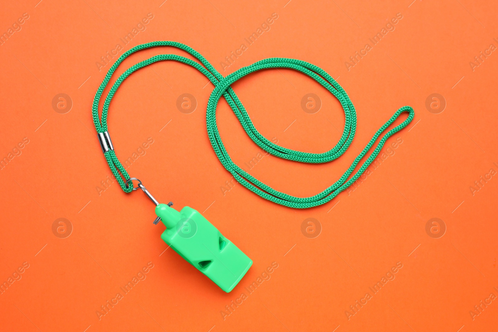 Photo of One green whistle with cord on orange background, top view