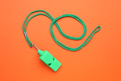 One green whistle with cord on orange background, top view