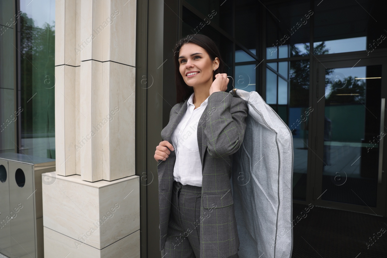 Photo of Attractive happy businesswoman holding garment cover with clothes outdoors. Dry cleaning service