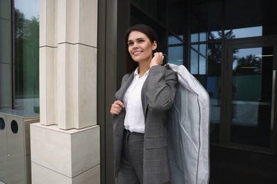 Attractive happy businesswoman holding garment cover with clothes outdoors. Dry cleaning service