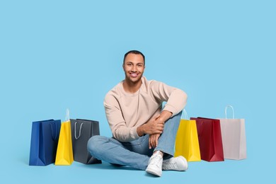 Happy African American man with shopping bags on light blue background