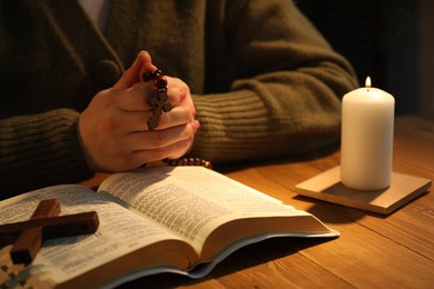 Woman praying at table with burning candle and Bible, closeup