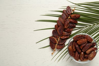 Photo of Tasty sweet dried dates and palm leaf on white wooden table, flat lay. Space for text